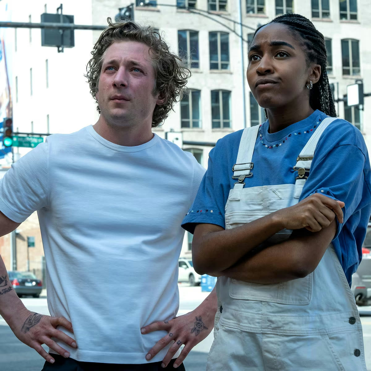 Carmy e Sydney lado a lado numa rua de Chicago, ele de camiseta branca e ela de azul e branco