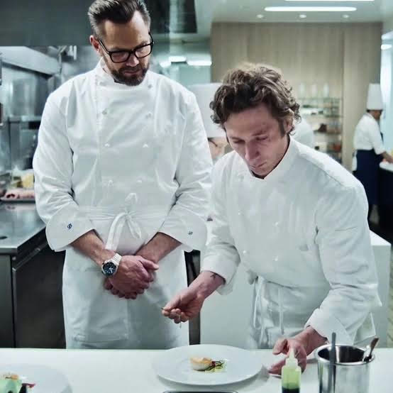 Carmy numa cozinha de alta gastronomia em Nova York, tudo branco, sendo observado pelo chefe