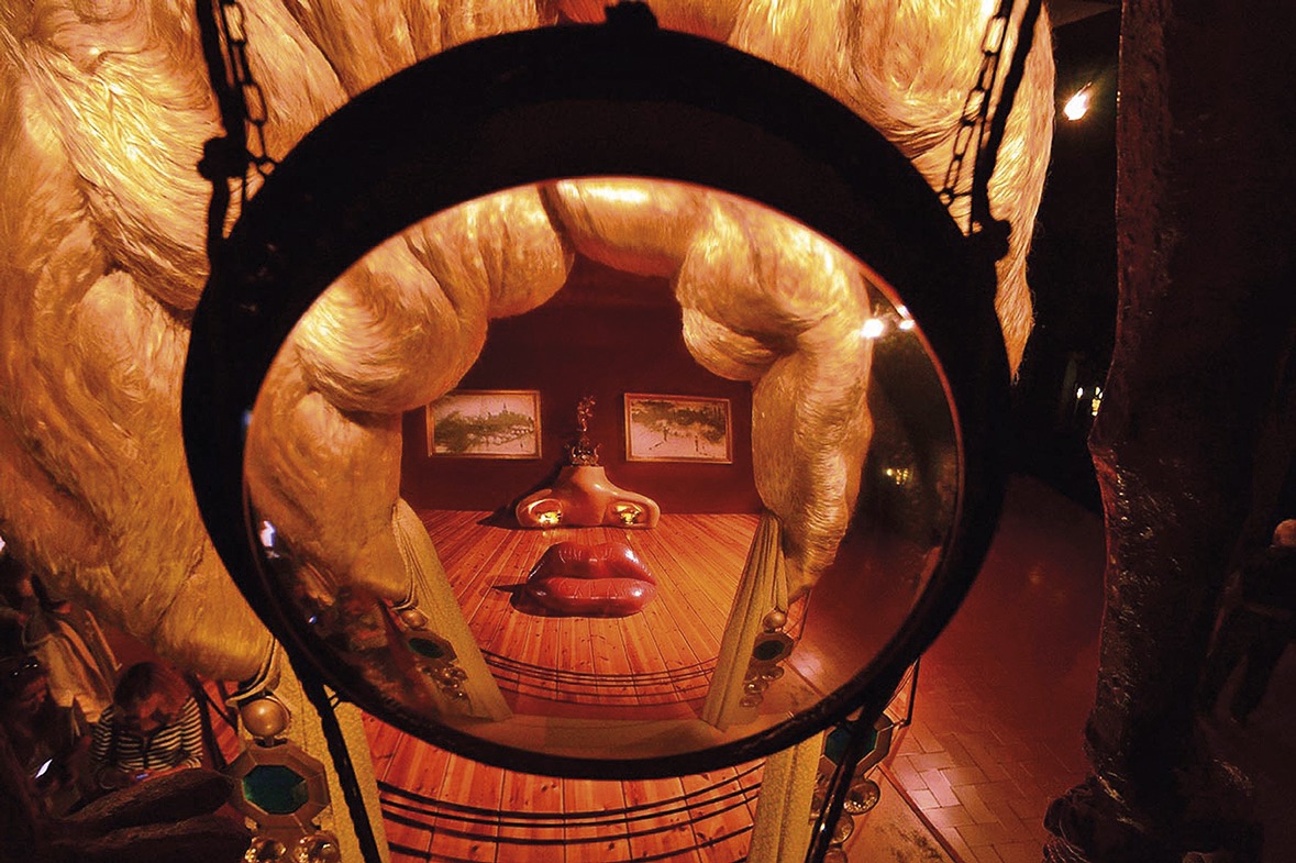 Instalação surrealista observada através de uma lente circular, formando um rosto dentro de uma sala